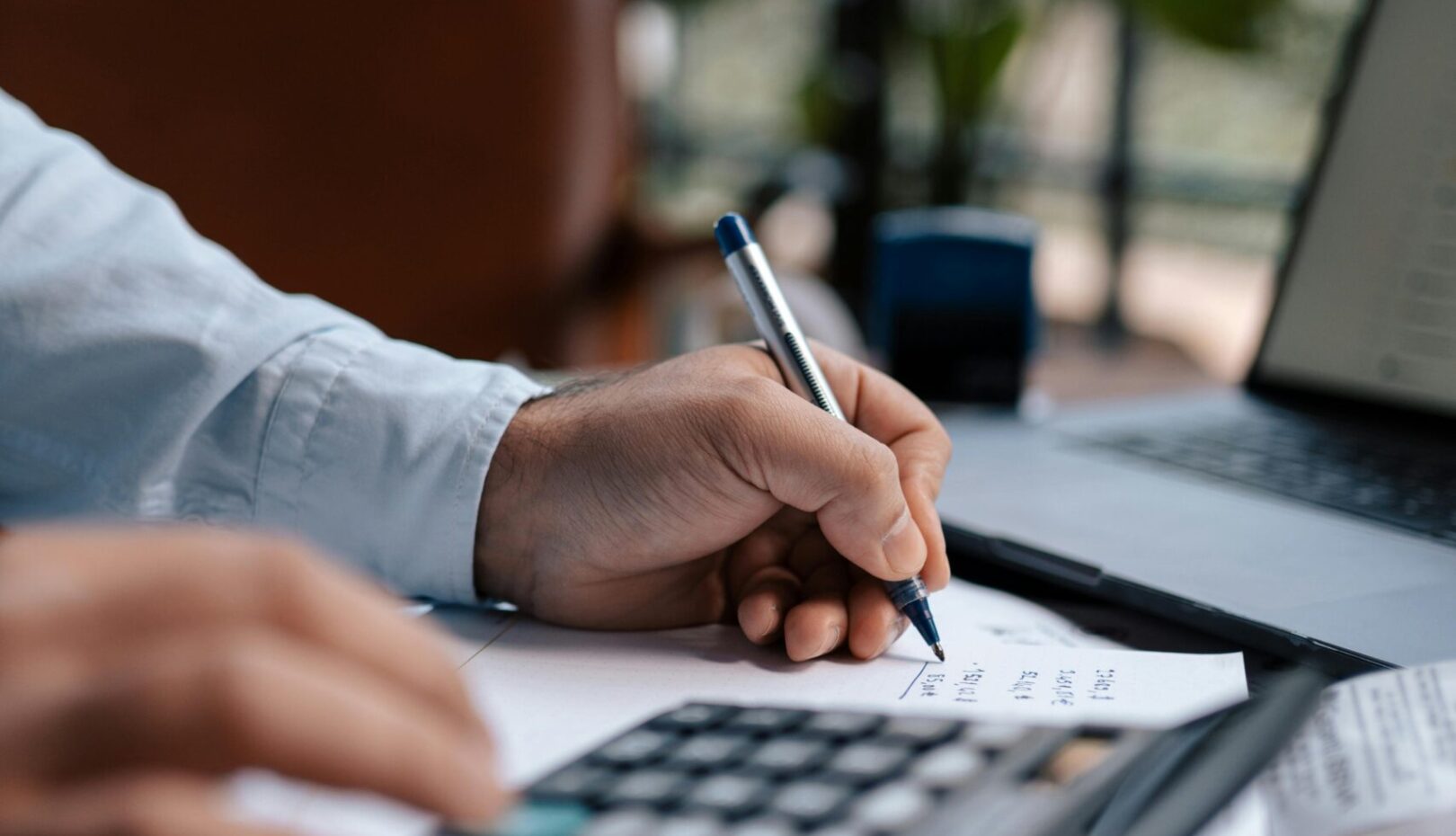 Free A person calculating finances with a calculator and pen on a desk indoors. Stock Photo